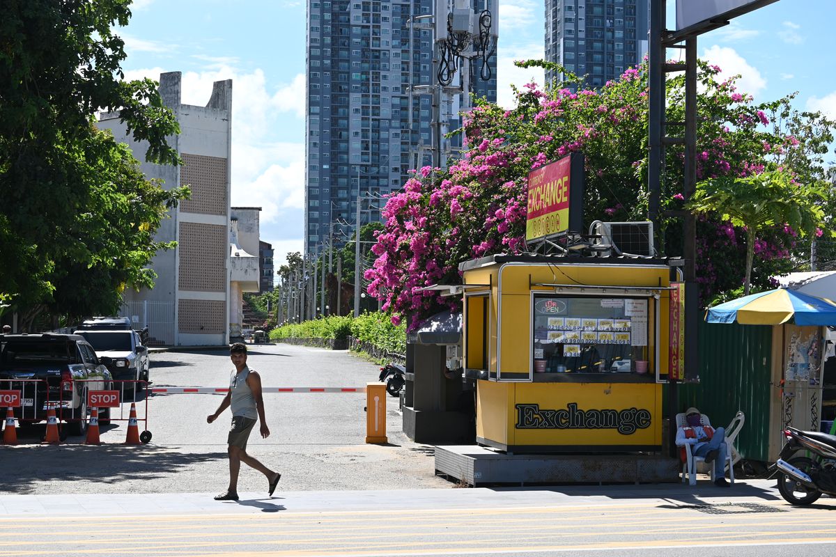 A yellow street currency exchange kiosk with a handwritten rate board on a city corner